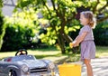 Cute gorgeous toddler girl washing big old toy car in summer garden, outdoors. Happy healthy little child cleaning car Royalty Free Stock Photo