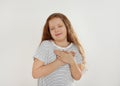 Cute grateful little girl with hands on chest against background