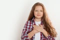 Cute grateful little girl with hands on chest against background