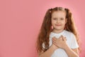 Cute grateful little girl with hands on chest against background. Space for text