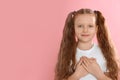 Cute grateful little girl with hands on chest against background. Space for text