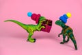 Green toy dinosaur in knitted hat give present box to another dinosaur in hat, festive funny greeting card