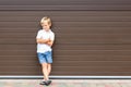 Cute grumpy blond child in casual clothing standing against brown garage door. Angry kid boy with crossed arms near house.Awkward Royalty Free Stock Photo