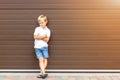 Cute grumpy blond child in casual clothing standing against brown garage door. Angry kid boy with crossed arms near house.Awkward Royalty Free Stock Photo