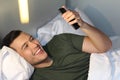 Cute guy comfortably using phone in bed Royalty Free Stock Photo