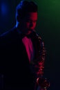 Cute Guy Musician Enjoys Playing the Saxophone, Tenor Saxophone. Neon Light. Selective focus. Close-up Portrait