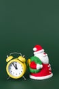 Cute gypsum colorful santa claus and yellow clock isolated over green background. New Year and Christmas concept. Royalty Free Stock Photo