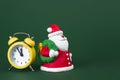 Cute gypsum colorful santa claus and yellow clock isolated over green background. New Year and Christmas concept. Royalty Free Stock Photo