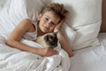 Cute handsome blonde boy lying in white bed. Boy smiling and playing with cat. Relax time Royalty Free Stock Photo