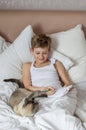 Cute handsome blonde boy lying in white bed and drawing. Boy smiling and playing with cat. Relax time Royalty Free Stock Photo