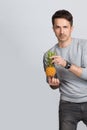 Handsome young man holding a small yellow pineapple in his hands and looking at the camera on a gray background. Royalty Free Stock Photo