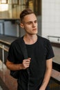 Cute handsome young man in a stylish black T-shirt with a stylish hairstyle with a backpack poses in the city Royalty Free Stock Photo