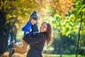 Cute, happy, boy smiling and hugging with his mom among yellow leaves. Little child having fun with mother in autumn park. Concept Royalty Free Stock Photo