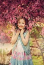 Cute happy child girl in jeans vest enjoying spring near blooming crab apple tree in country garden Royalty Free Stock Photo