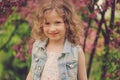 Cute happy child girl in jeans vest enjoying spring near blooming crab apple tree in country garden Royalty Free Stock Photo