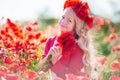 Cute happy blonde child girl is wearing wreath from red flowers in poppy field Royalty Free Stock Photo