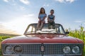 Cute happy children boy in grey t-shirt and girl in blue striped dress sitting together on the roof of the red retro car Royalty Free Stock Photo