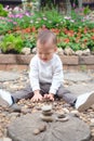 Cute happy & curious little Asian 1 year / 18 months old toddler baby boy child sitting on in the beautiful flowers garden holding Royalty Free Stock Photo