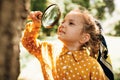 Cute happy kid with magnifying glass exploring the nature outdoor. Adorable little explorer girl playing in forest with magnifying Royalty Free Stock Photo