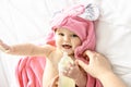 A Cute happy laughing baby in soft bathrobe after bath playing on white bed in pink Royalty Free Stock Photo