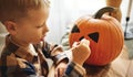 Little kid boy making jack-o-lantern at home, drawing scary face on pumpkin