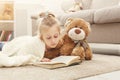 Happy little female child and her teddy bear reading book on the floor at home Royalty Free Stock Photo