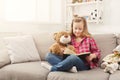 Happy little female child hugging her teddy bear and reading book on sofa at home Royalty Free Stock Photo