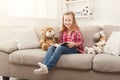 Happy little female child hugging her teddy bear and reading book on sofa at home Royalty Free Stock Photo