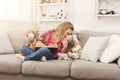 Happy little female child hugging her teddy bear and reading book on sofa at home Royalty Free Stock Photo