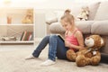 Happy little female child and her teddy bear reading book on the floor at home Royalty Free Stock Photo