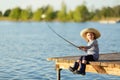 Cute happy little child girl in rubber boots fishing from wooden pier on a lake. Family leisure activity during summer sunny day Royalty Free Stock Photo