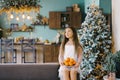 A cute happy little girl in a beautiful white dress is sitting on the sofa next to a Christmas tree with tangerines. Christmas Royalty Free Stock Photo