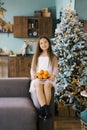 A cute happy little girl in a beautiful white dress is sitting on the sofa next to a Christmas tree with tangerines. Christmas Royalty Free Stock Photo