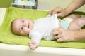 Cute happy little girl getting dressed. Mother dressing her baby on changing pad. Infant baby with diaper. Royalty Free Stock Photo