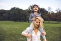 Cute happy little girl laughing and sitting on her beautiful mother`s shoulders have fun outdoor in the park. Happy family time Royalty Free Stock Photo