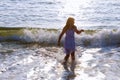 Cute happy little girl running along the beach in jumping over waves. Beautiful summer sunny day, blue sea, picturesque landscape. Royalty Free Stock Photo