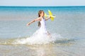 Cute happy little girl wearing a white dress running through the sea water and playing with the yellow toy pl Royalty Free Stock Photo