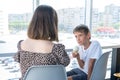 A cute happy little schoolboy boy is talking to his mother sitting at a table in a cafe against window. Mom talks to her Royalty Free Stock Photo