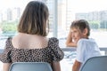 A cute happy little schoolboy boy is talking to his mother sitting at a table in a cafe against window. Mom talks to her Royalty Free Stock Photo