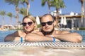 Cute happy loving caucasian couple in a swimming pool in tropical resort outdoors smiling in sunglasses. Lifestyle. Copy space