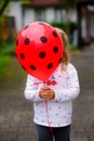 Cute happy preschool girl playing with ladybug balloon outdoors. Little child celebrating birthday. Royalty Free Stock Photo