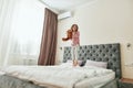 A cute happy small girl is having fun jumping on a big bed with her teddy bear Royalty Free Stock Photo