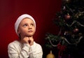 Cute happy smiling girl in fur santa claus hat near the Christmas holiday tree asking, dreaming the gift and looking up. Closeup Royalty Free Stock Photo