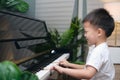 Cute happy smiling little Asian kid boy playing piano in living room at home, Preschool child having fun with learning to play Royalty Free Stock Photo