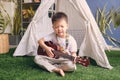 Cute happy smiling little Asian kindergarten boy child having fun playing Hawaiian guitar or ukulele in front of play tent at home Royalty Free Stock Photo