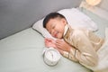 Cute happy smiling little Asian boy kid in pajama taking a nap, sleeping in bed with alarm clock Royalty Free Stock Photo