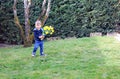 Cute happy smiling little boy in blue vest holding bouquet of bright yellow daffodils flowers staying on green grass