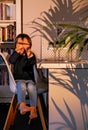 Cute happy toddler boy playing hide and seek hiding his face behind hands sitting on chair in hard warm sunset light