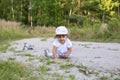 Cute happy toddler in a cap crawls on all fours along a country road in the sand on a sunny summer day Royalty Free Stock Photo