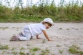 Cute happy toddler in a cap crawls on all fours along a country road in the sand on a sunny summer day Royalty Free Stock Photo